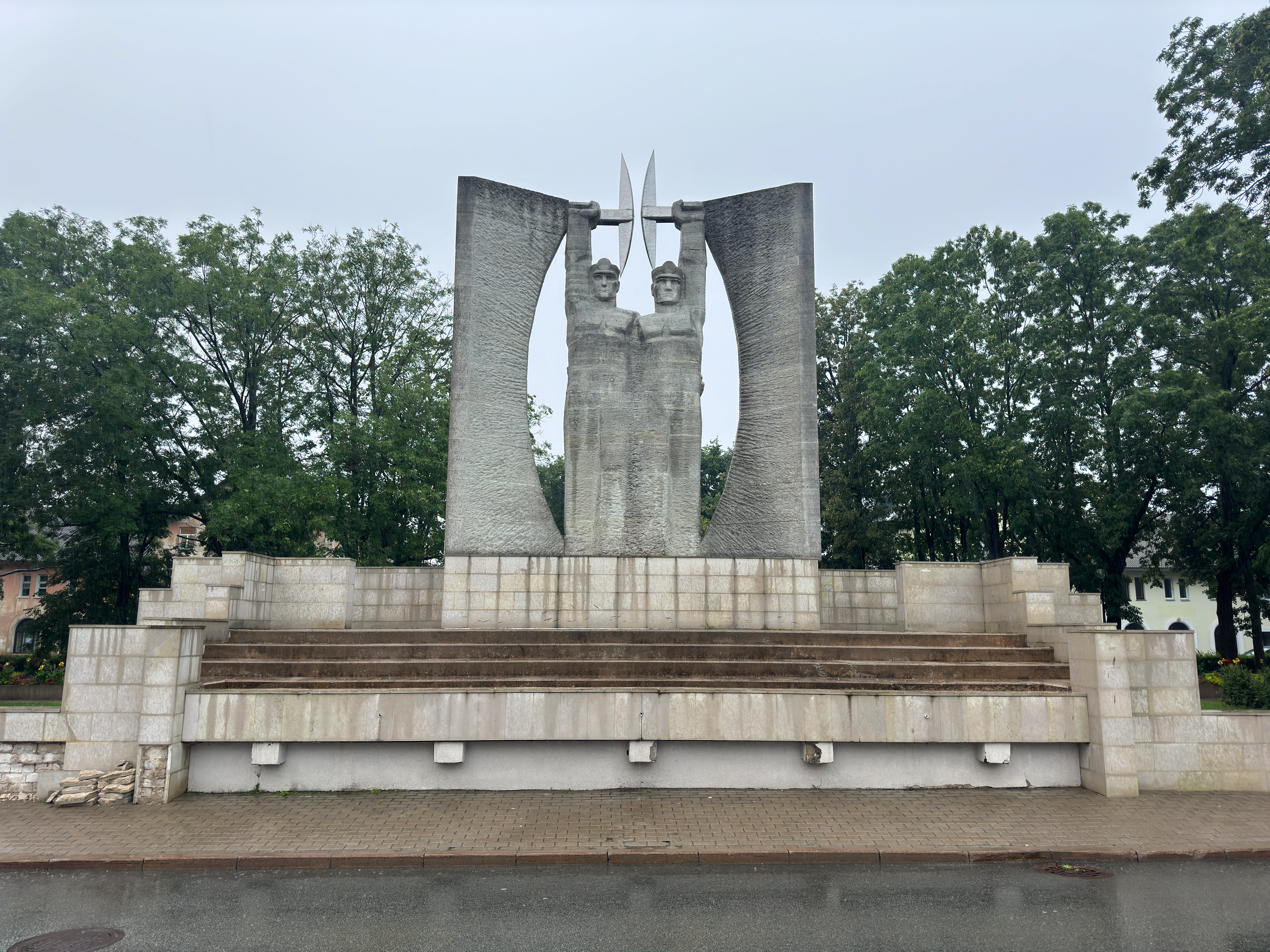 Close-up of the brutalist concrete Glory to Work monument in Kohtla-Järve, detailing the upper bodies and determined faces of two sculpted miners holding pickaxes aloft.