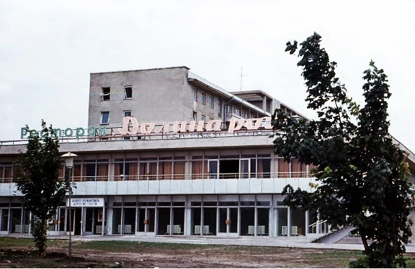 Color photograph of the exterior of the "Valley of the Roses" restaurant building attached to the Gagarin Youth Center complex in Chisinau in 1972, featuring a flat roof topped with large Cyrillic neon letters spelling the restaurant's name, floor-to-ceiling glass doors, and an exterior concrete staircase.