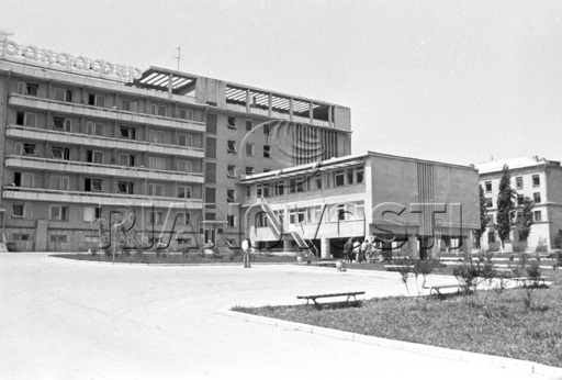 Black and white 1972 architectural photograph of the "Trandafir" tourist hotel building located within the Gagarin Youth Center complex in Chisinau, showing a multi-story Soviet modernist block with a grid of balconies, large rooftop Cyrillic signage, and a lower adjoining structure elevated on concrete pillars.