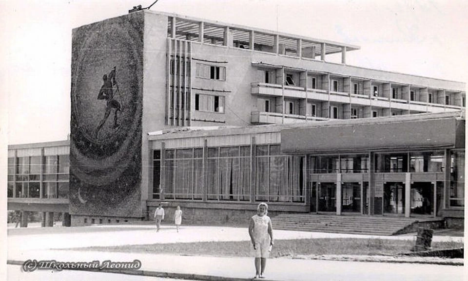Wide-angle black and white historical photograph from 1972 showing the newly opened Gagarin Youth Center in Chisinau, capturing the main entrance with wide steps, the long glass facade, the striking "Plowman of the Universe" side mosaic, and pedestrians walking across the spacious paved entrance square.