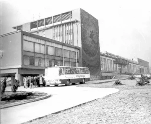 Early black and white historical photograph of the Gagarin Youth Center exterior in Chisinau featuring the modernist architectural design, a long glass facade, large Cyrillic rooftop lettering, and a parked Sputnik tourist bus dropping off visitors near the main entrance.